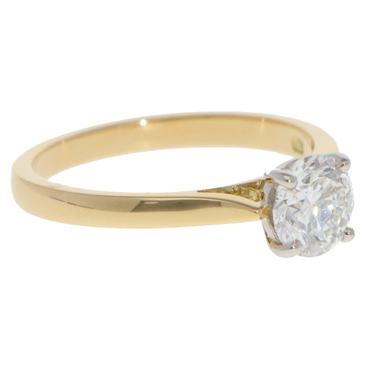 A yellow gold and platinum solitaire brilliant cut diamond ring, on a white background
