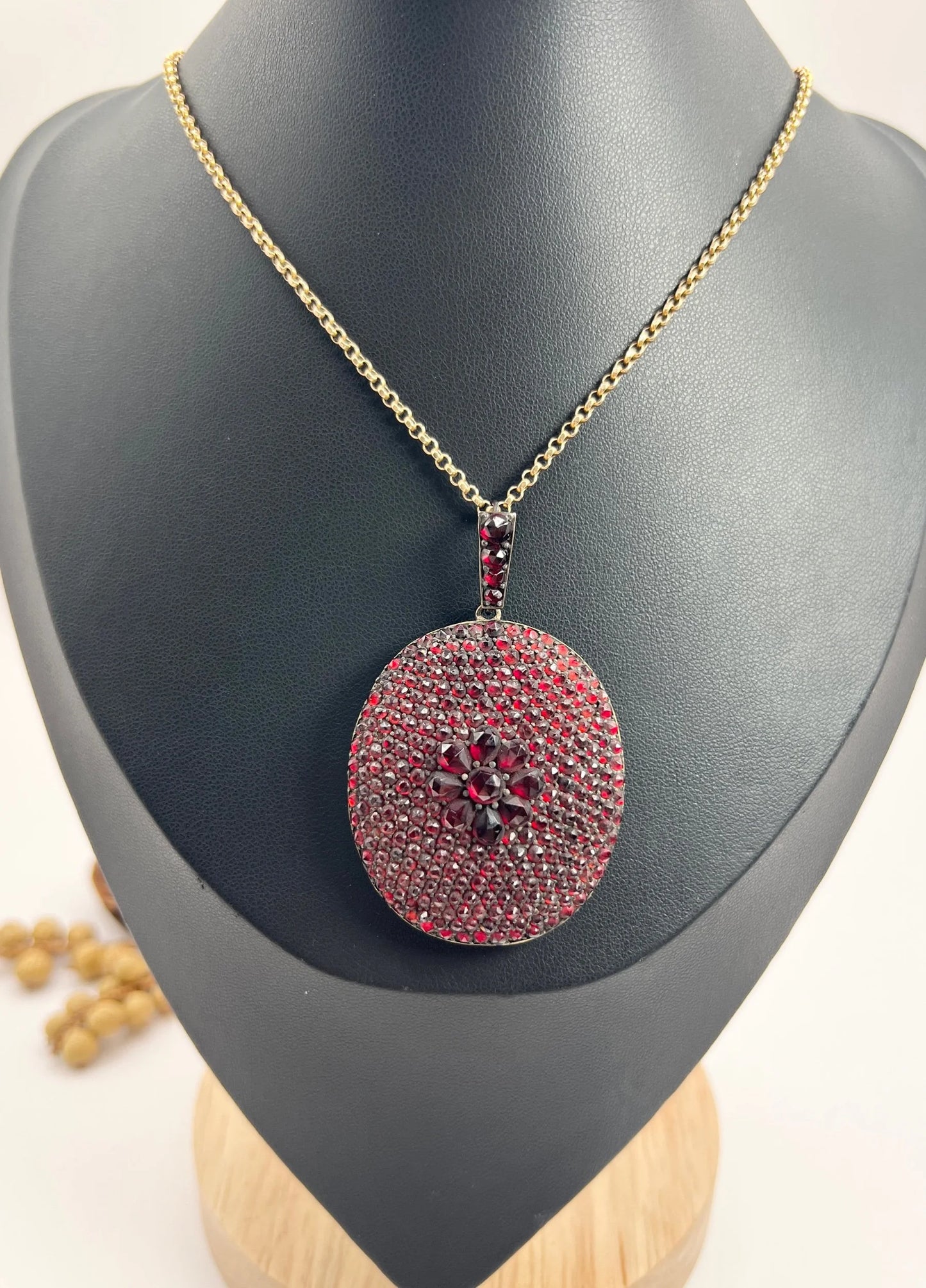 An antique oval locket encrusted with garnets, with a chain, on a black bust