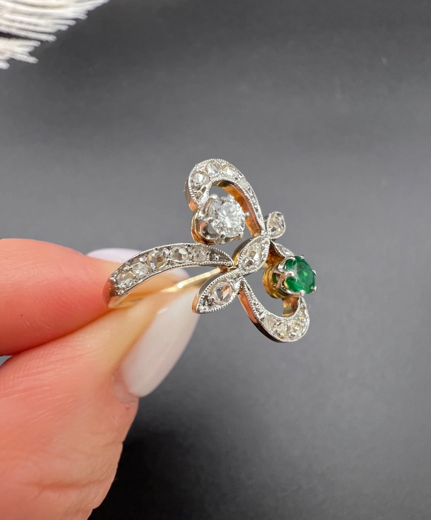 An emerald and diamond fancy openwork ring in yellow gold and platinum, held in a hand