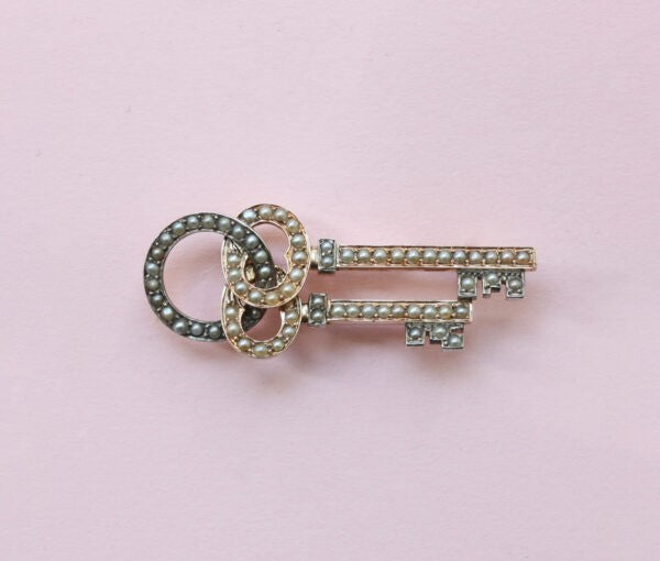 Antique Victorian Natural Pearl and 15ct Gold Key Brooch; two intertwined keys set with natural half pearls, and suspended from a keyholder. England, Circa 1880