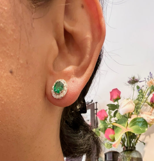 An oval cluster stud earring with green garnet and white diamonds, modelled in an ear