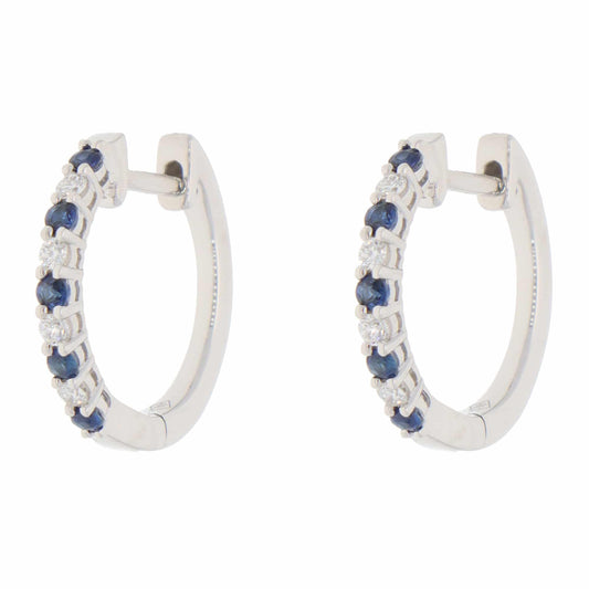A pair of white gold hoop earrings set with round sapphires and diamonds, on a white background