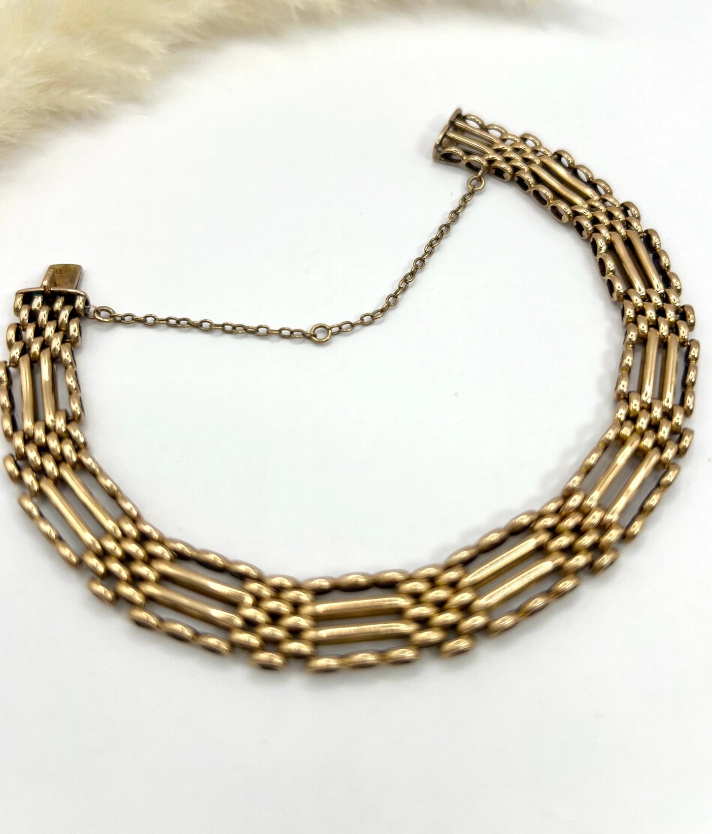 A yellow gold gate bracelet, laid flat on a white background