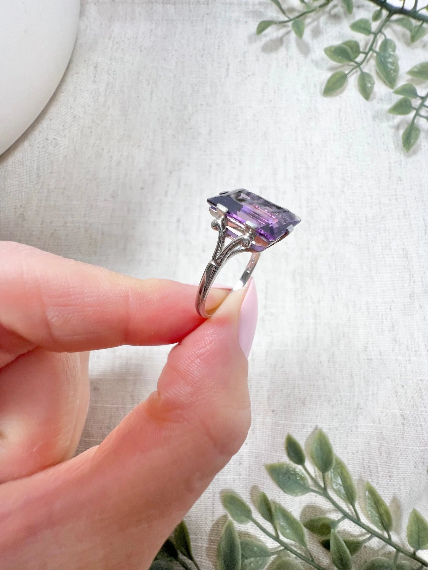 A solitaire amethyst cocktail ring in platinum, held in a hand