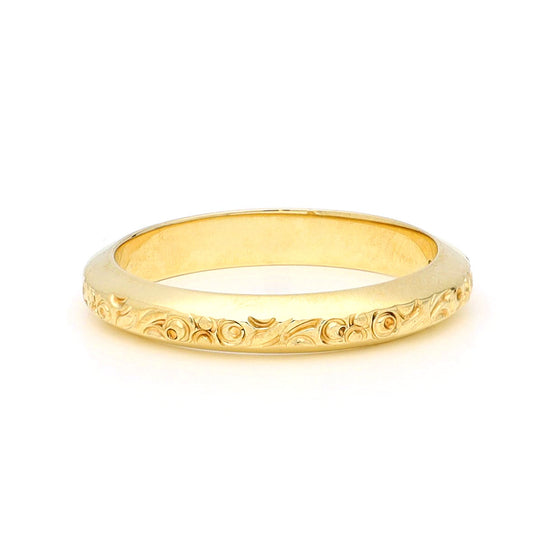 A yellow gold engraved band ring, against a white background