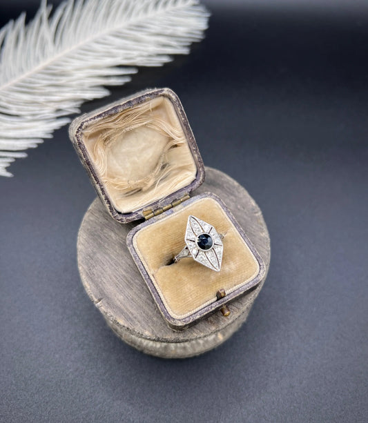 A navette shaped cluster cocktail ring with a sapphire centre surrounded by diamonds, in platinum, in an antique ring box