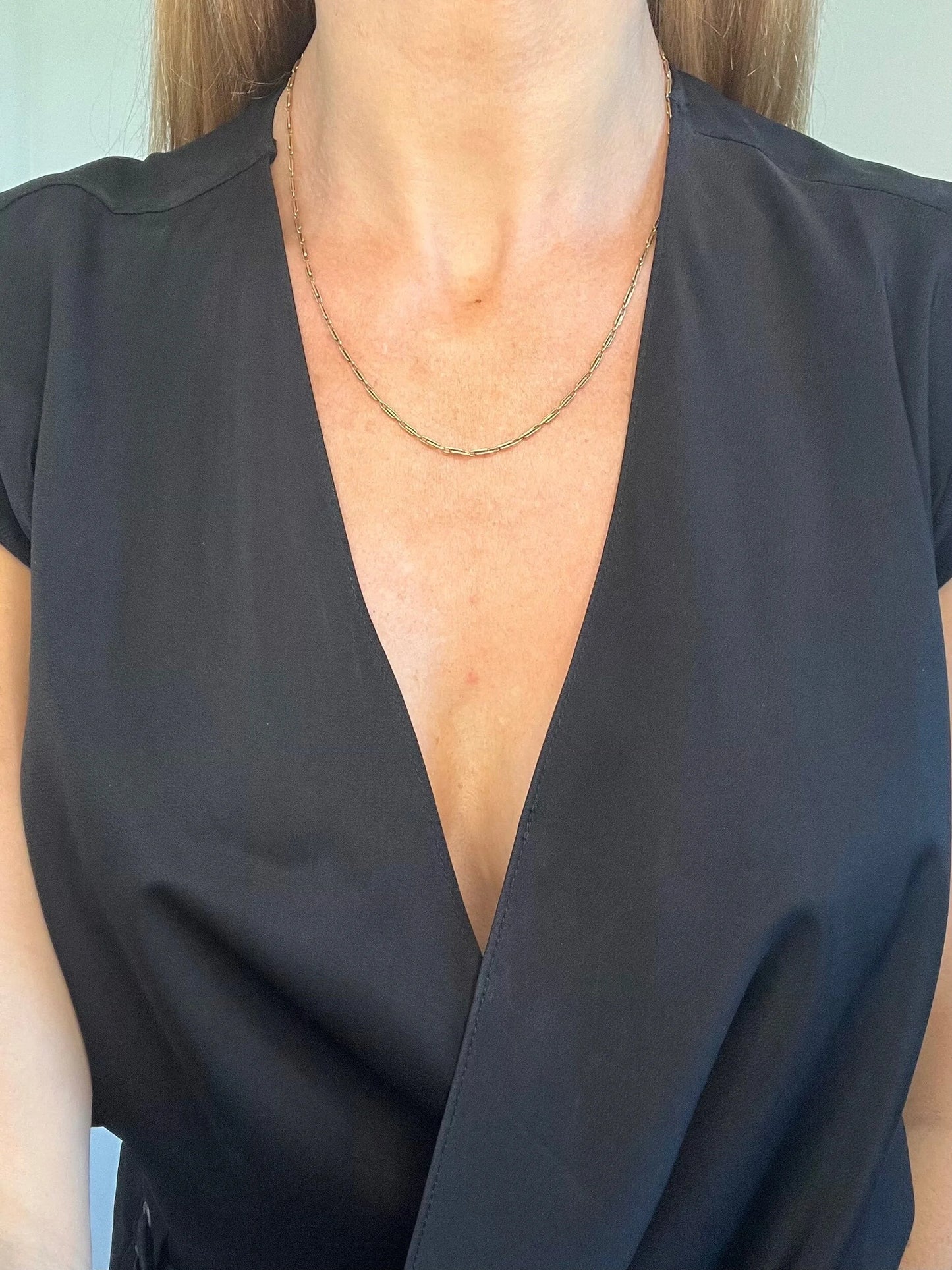 A gold paperclip link chain necklace, modelled by a woman