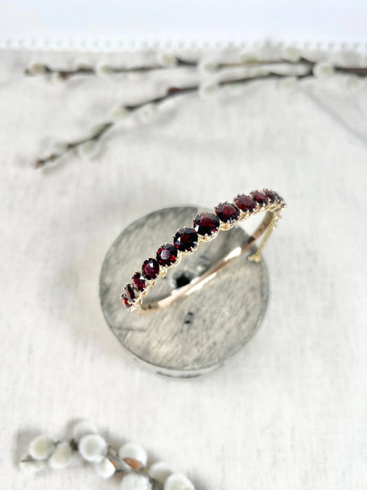 A yellow gold garnet bangle bracelet, on top of a wooden spool