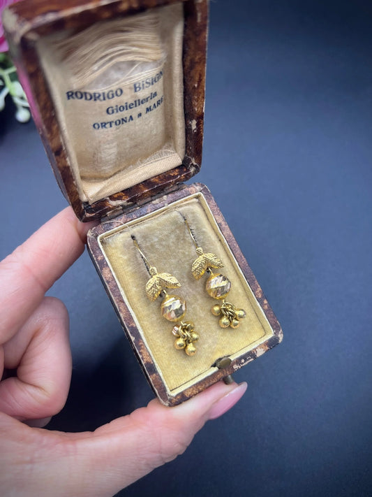 A pair of yellow gold leaf and faceted ball drop earrings with hook fittings, in an antique box, held in a hand