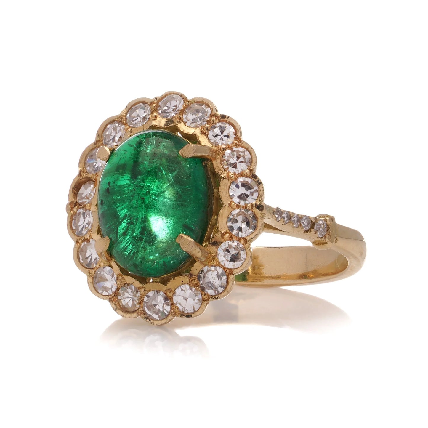 A yellow gold ring with an oval emerald surrounded by round diamonds, on a white background