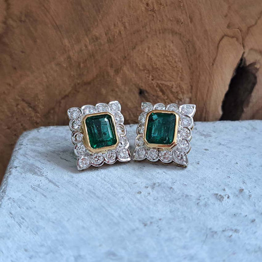 A pair of emerald and diamond rectangular cluster earrings in yellow and white gold, on a textured countertop