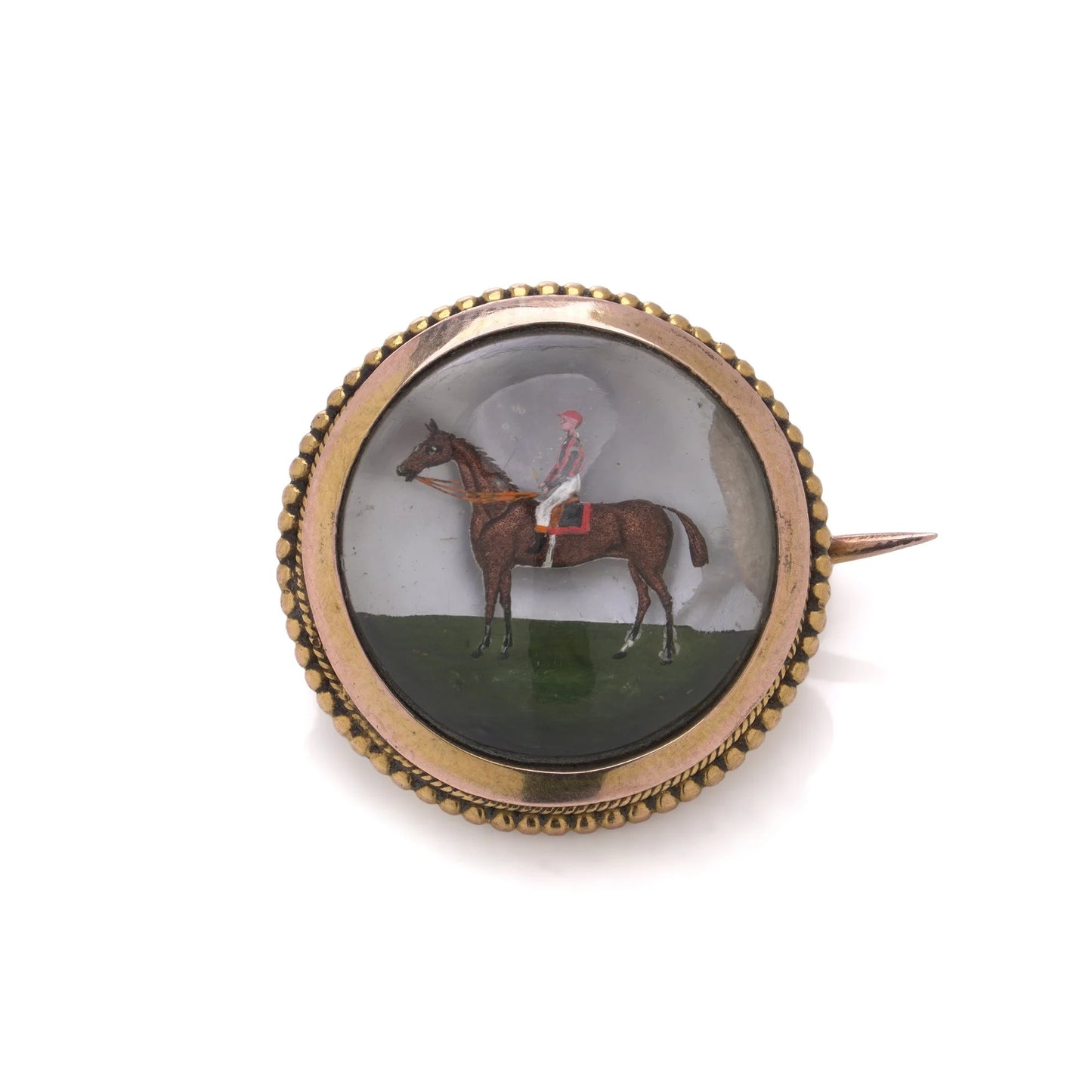 A round crystal brooch in yellow gold featuring a jockey sitting on a horse's back, on a white background