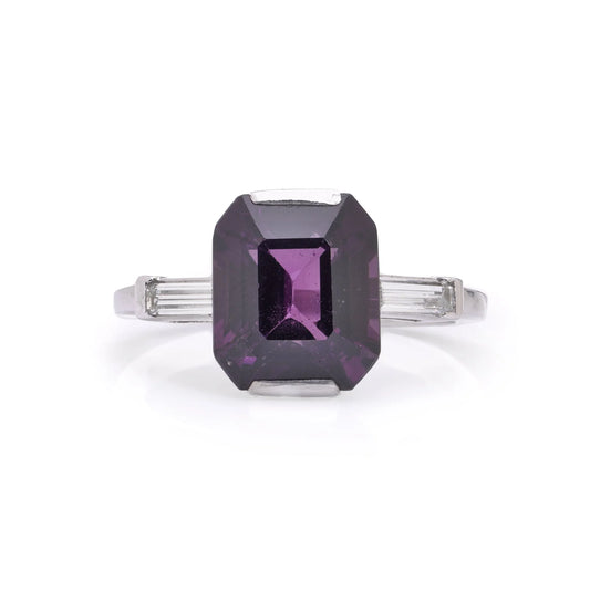An octagonal cut purple spinel ring with baguette cut diamond shoulders in white metal, on a white background
