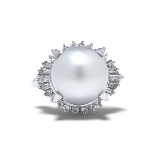 A platinum ring featuring a large white pearl surrounded by baguette and brilliant cut diamonds, on a white background