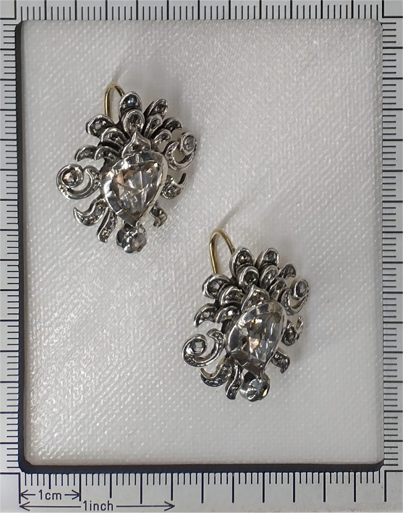 A pair of rose-cut diamond ornate earrings in silver and gold, next to a ruler