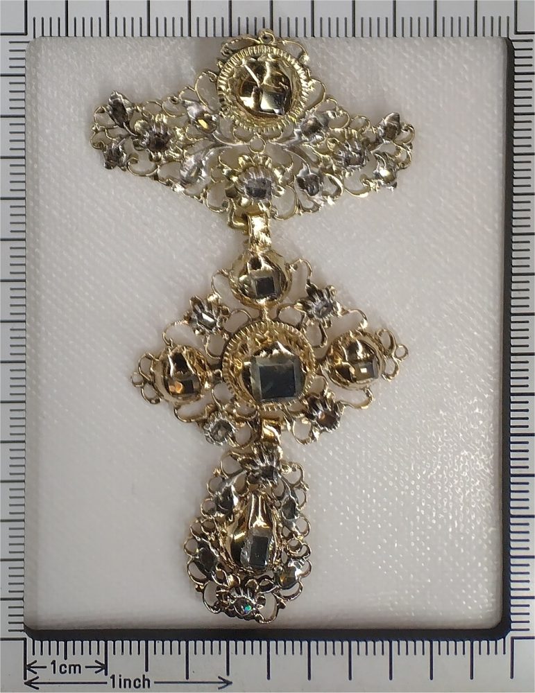 An ornate cross pendant in gold and silver with antique cut diamonds next to a ruler