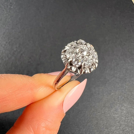 A round diamond cluster ring in white gold, held in a hand