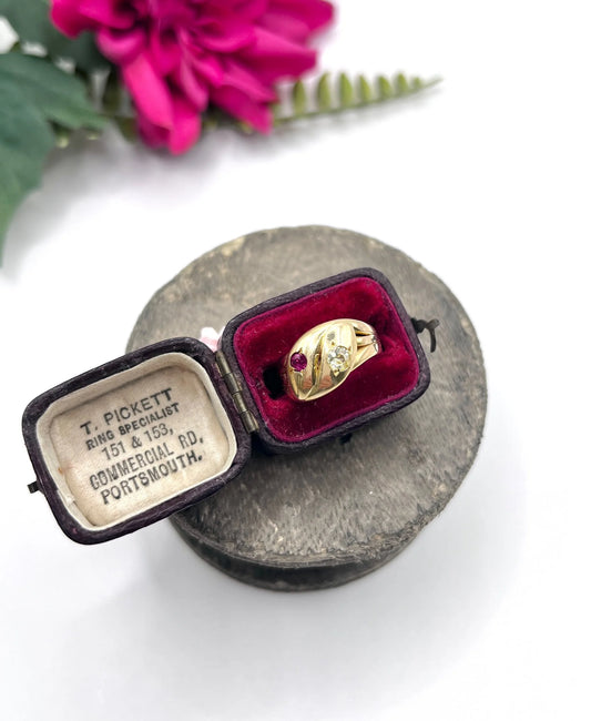 A yellow gold double headed snake ring with a ruby and a diamond, in a ring box