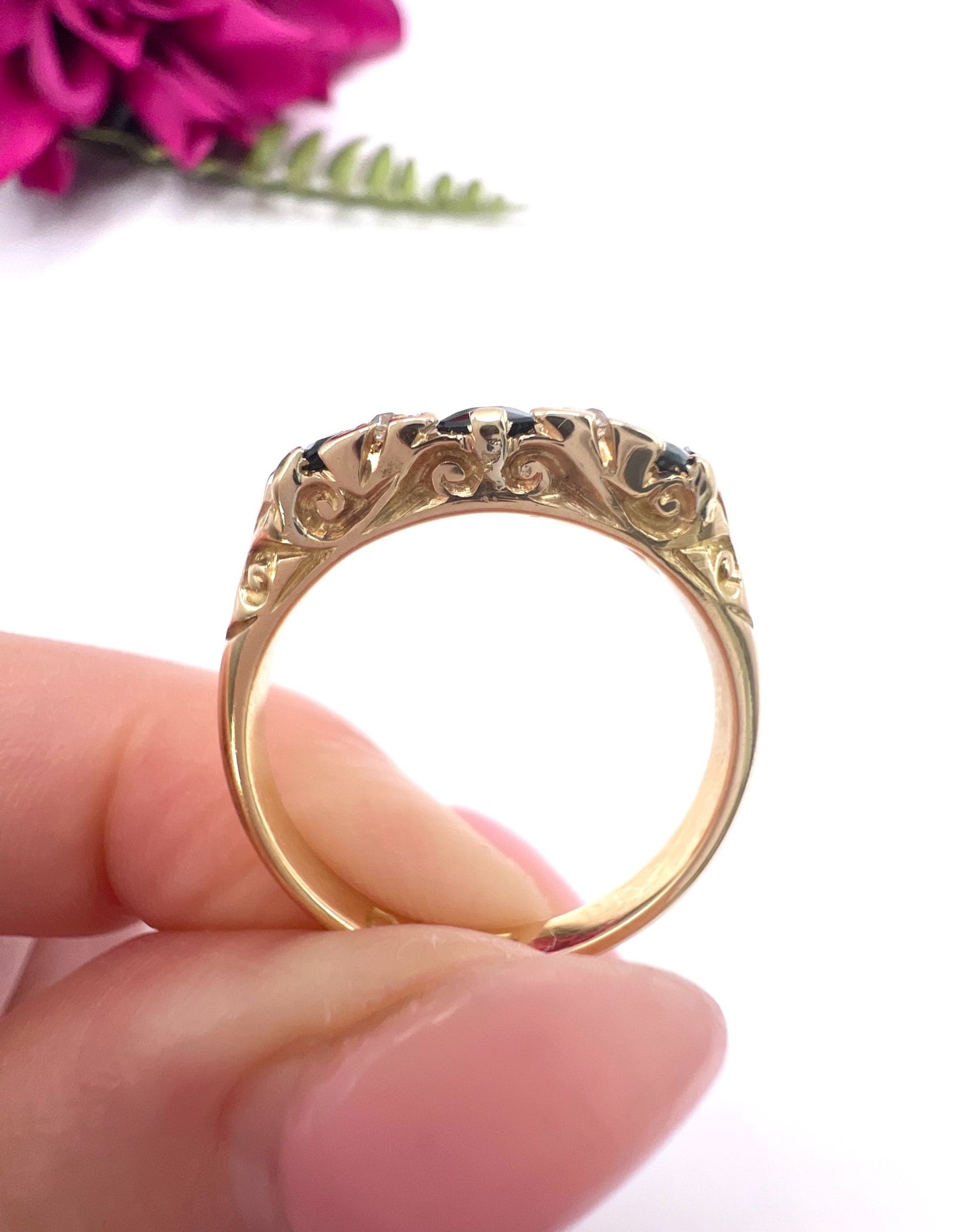A seven stone sapphire and diamond carved ring in yellow gold, held in a hand