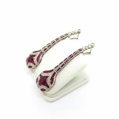 Art Deco Style Ruby, Diamond and Platinum Drop Earrings; featuring oval faceted rubies surrounded by calibre cut rubies and brilliant-cut diamonds set in a geometric design, suspended from an articulated graduated ruby and diamond set drop