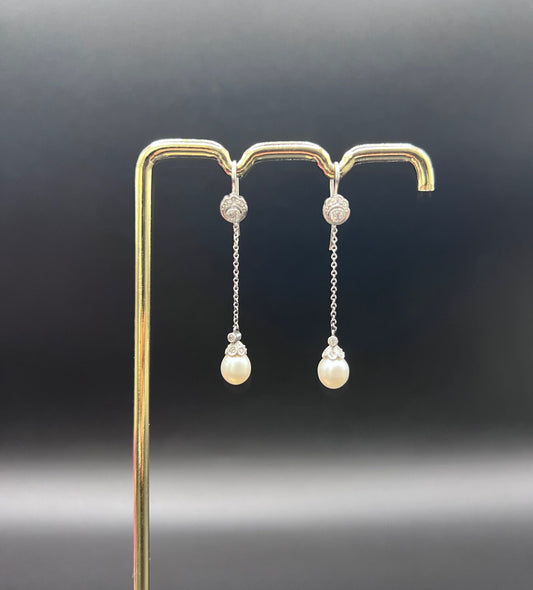 A pair of long drop platinum earrings with pearls and diamonds, on a gold hook