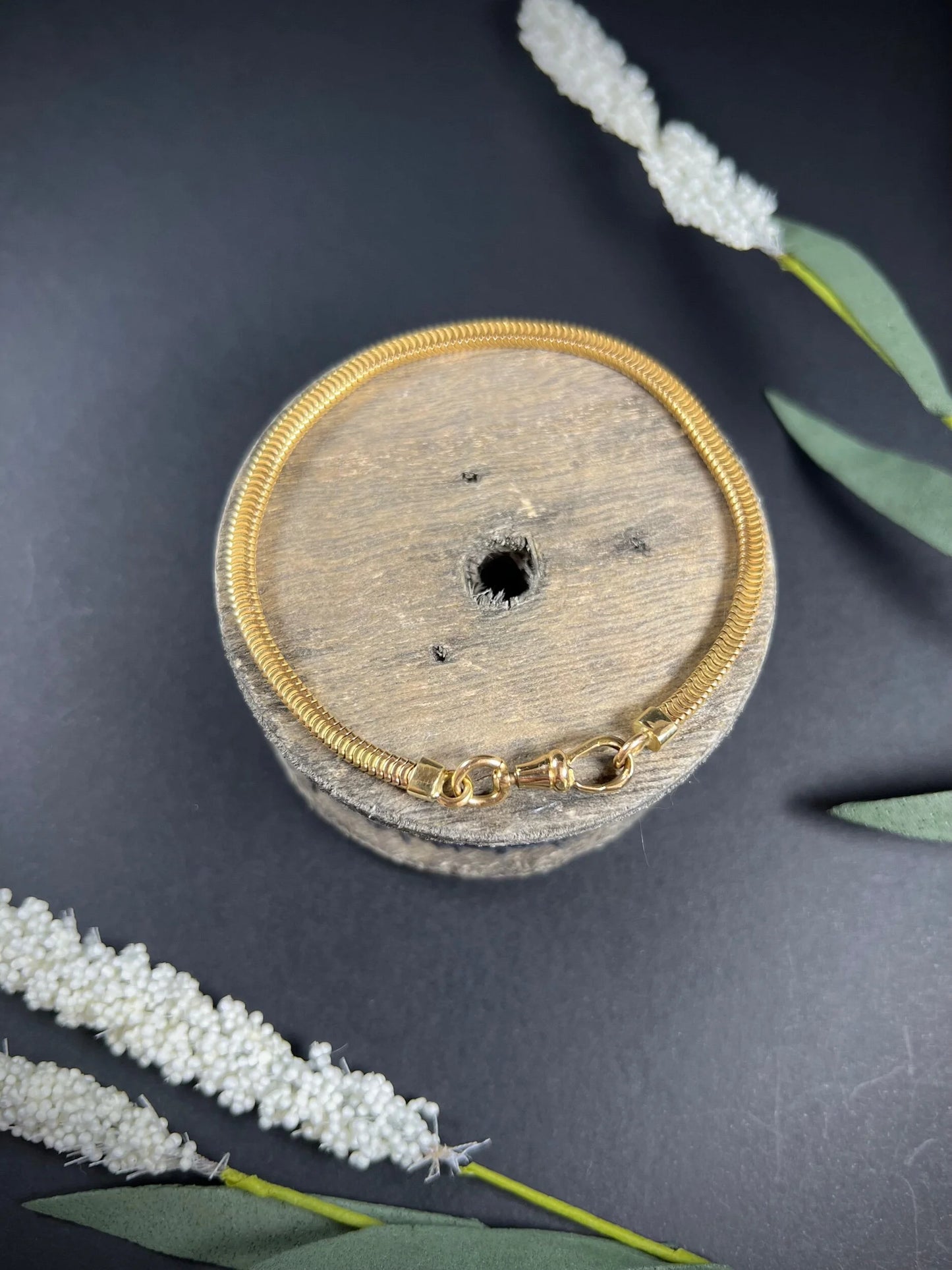 A yellow gold snake link bracelet, laid on a wooden spool