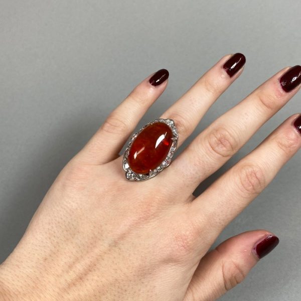 Cabochon Fire Opal and Diamond Cluster Ring in Platinum; central 18.00 carat oval shaped cabochon-cut fire opal, surrounded by 2.40cts brilliant and pear-cut diamonds