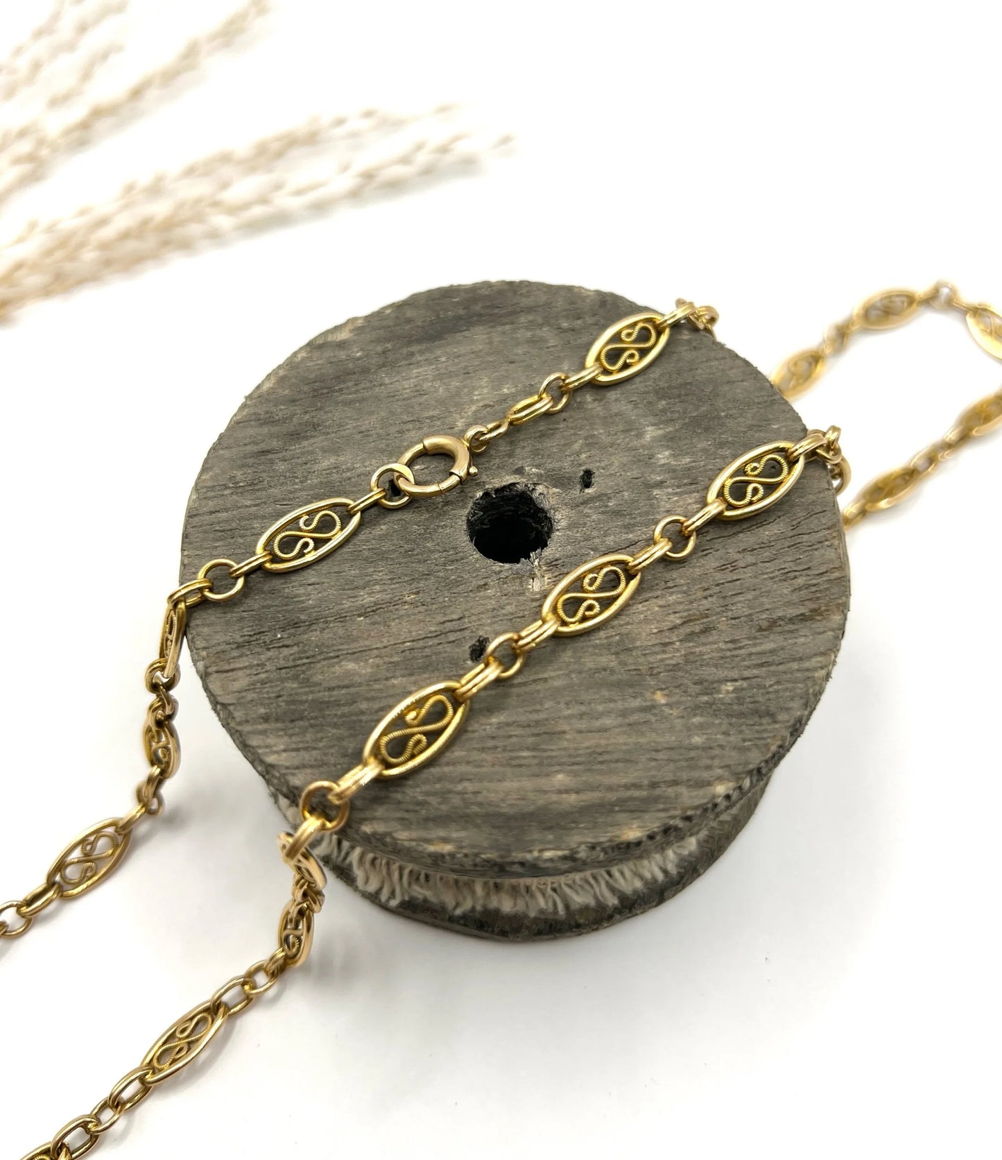 A yellow gold fancy link chain lying on a wooden object, on a white background