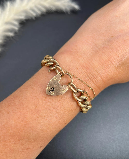 A rose gold curb link bracelet with heart padlock clasp and safety chain, modelled on a wrist