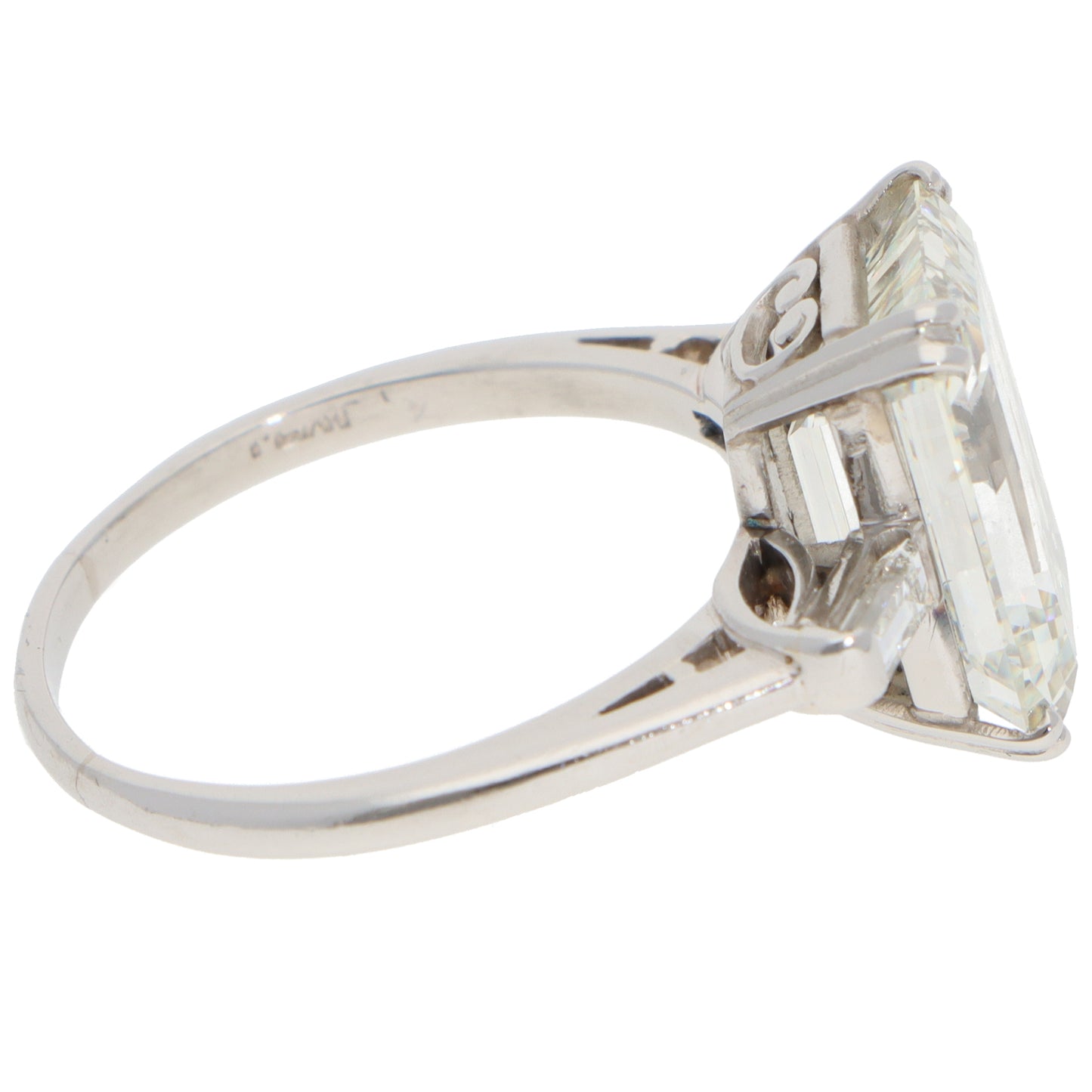 A large emerald cut diamond ring with baguette cut diamond shoulders in white metal, on a white background