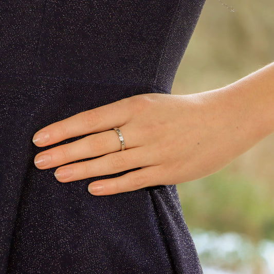 A white gold brilliant cut diamond eternity band, modelled by a woman wearing a black dress