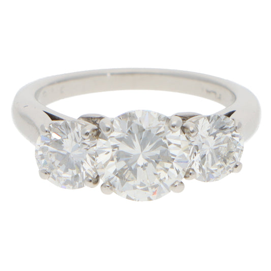 A three stone brilliant cut diamond claw set ring in white metal, on a white background