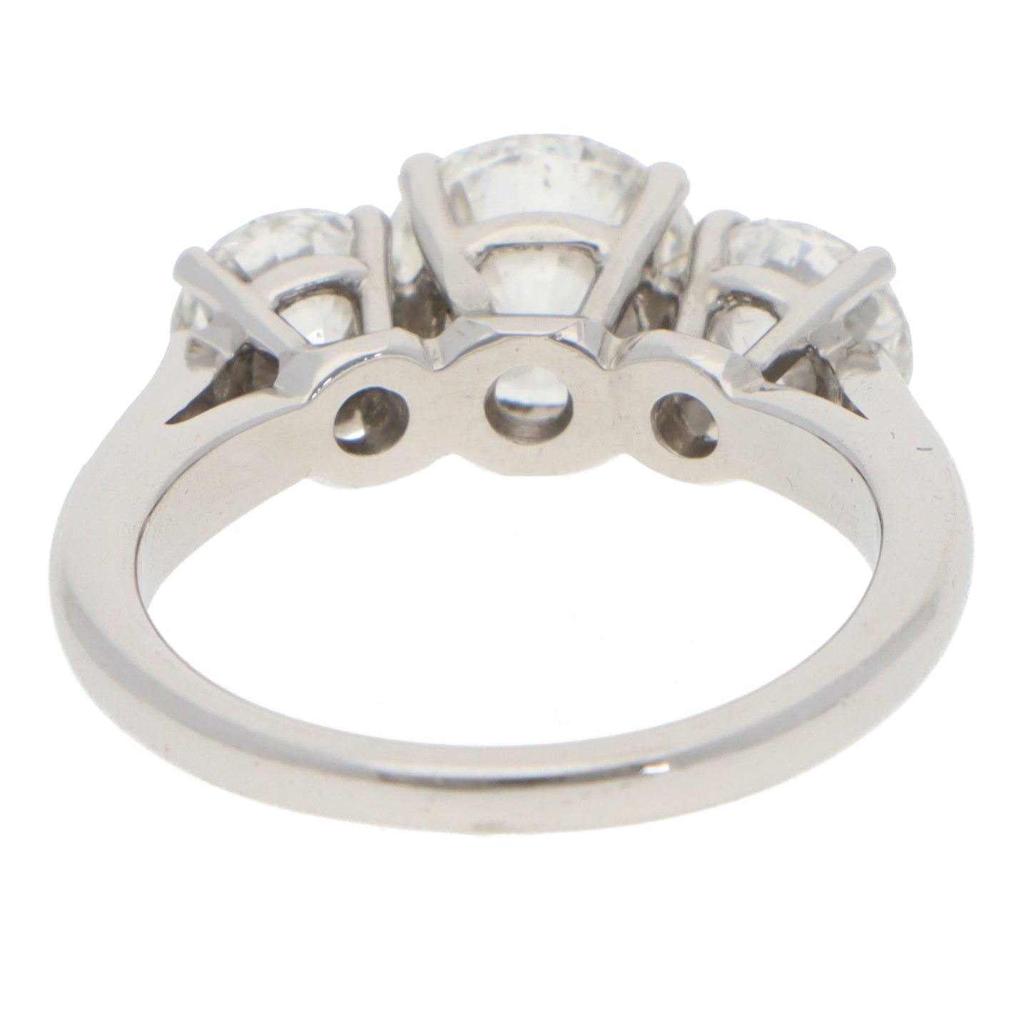 A three stone brilliant cut diamond claw set ring in white metal, on a white background