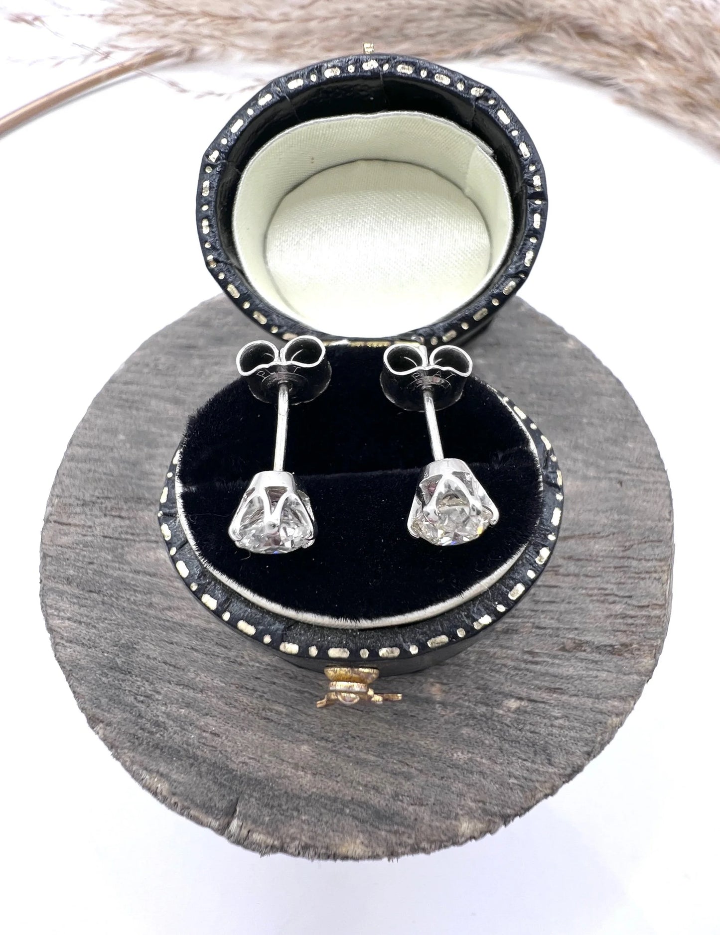 A pair of single stone round diamond stud earrings claw set in platinum, in a black jewellery box