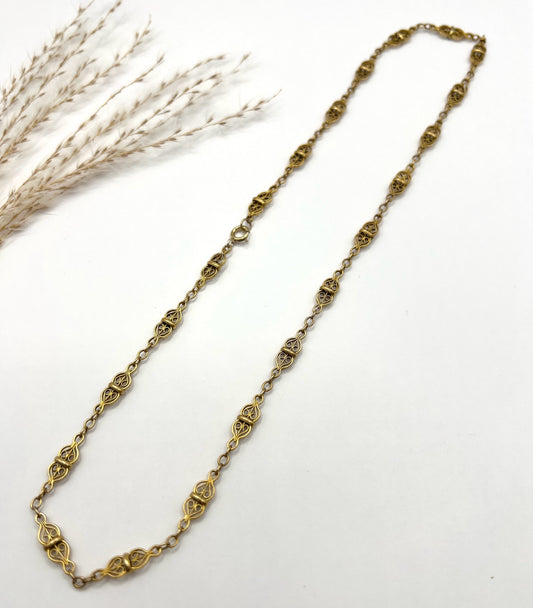 A yellow gold fancy link chain, laid flat on a white background