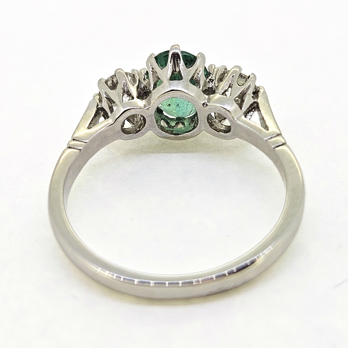 A platinum emerald and diamond three stone ring, viewed from behind, on a white background