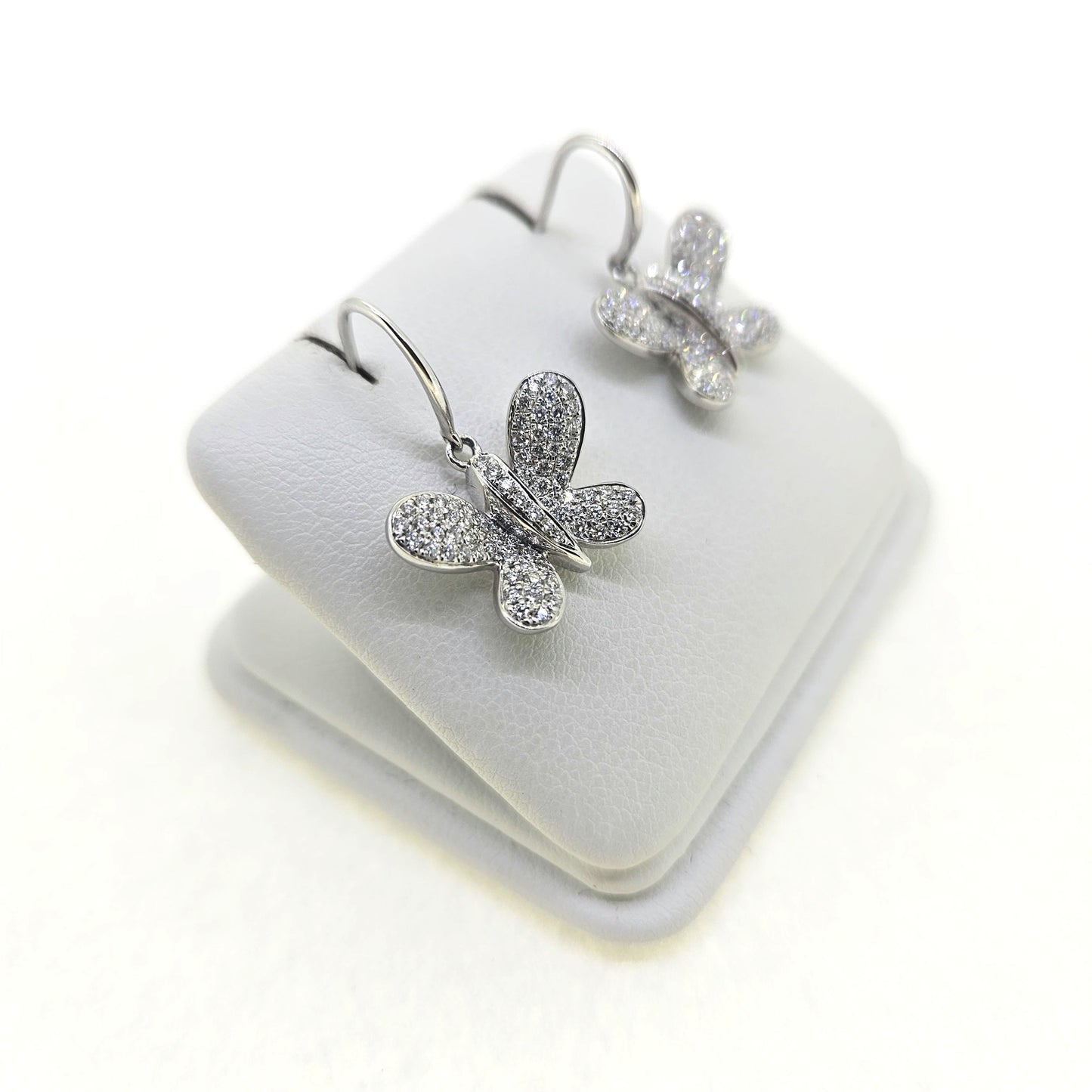 A pair of butterfly shaped diamond set earrings with hook fittings in white gold, on a white background