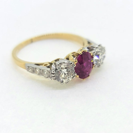 A three stone ruby and diamond ring in yellow and white gold, against a white background