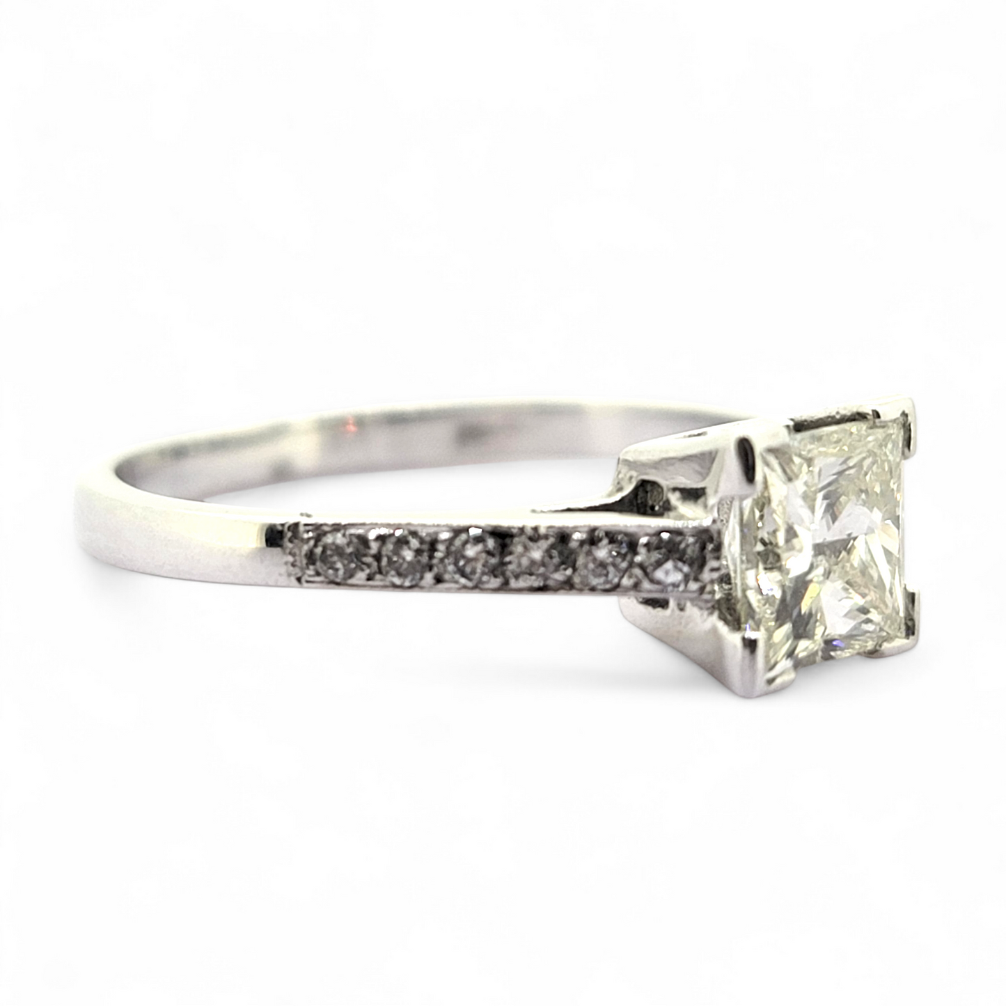 A princess cut diamond solitaire ring with diamond shoulders, in white gold, on a white background