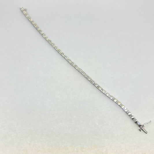A baguette cut diamond line bracelet in white gold, against a white background