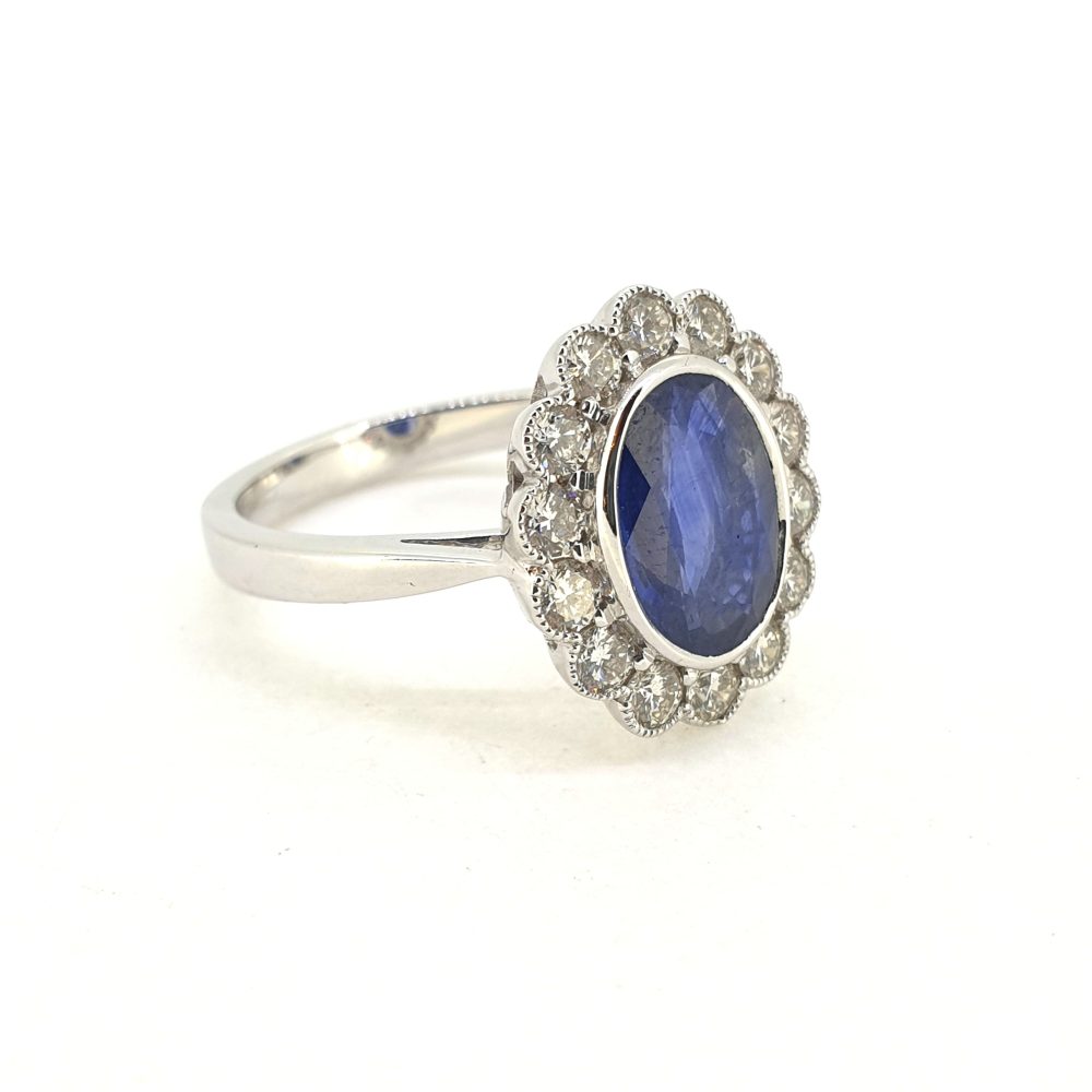 An oval sapphire and brilliant cut diamond cluster ring in white gold, against a white background