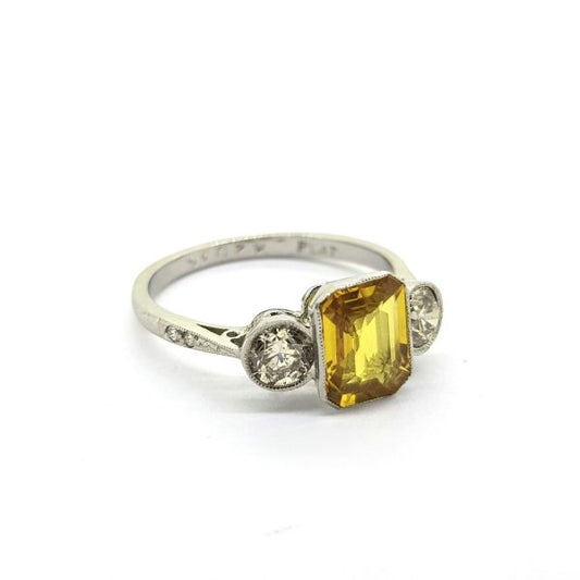 Yellow Sapphire and Diamond Three Stone Ring in Platinum; 1.80ct emerald-cut yellow sapphire flanked by round brilliant cut diamonds, diamond set shoulders