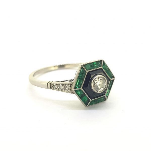 Vintage Art Deco Style Emerald, Diamond and Onyx Ring; 0.20ct J colour VVS1 Old European cut diamond framed with calibre cut emeralds and onyx, decorated with small single cut diamonds to the shoulders, in platinum. Circa 1960s
