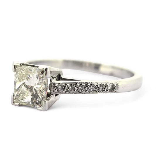 A princess cut diamond solitaire ring with diamond shoulders, in white gold, on a white background