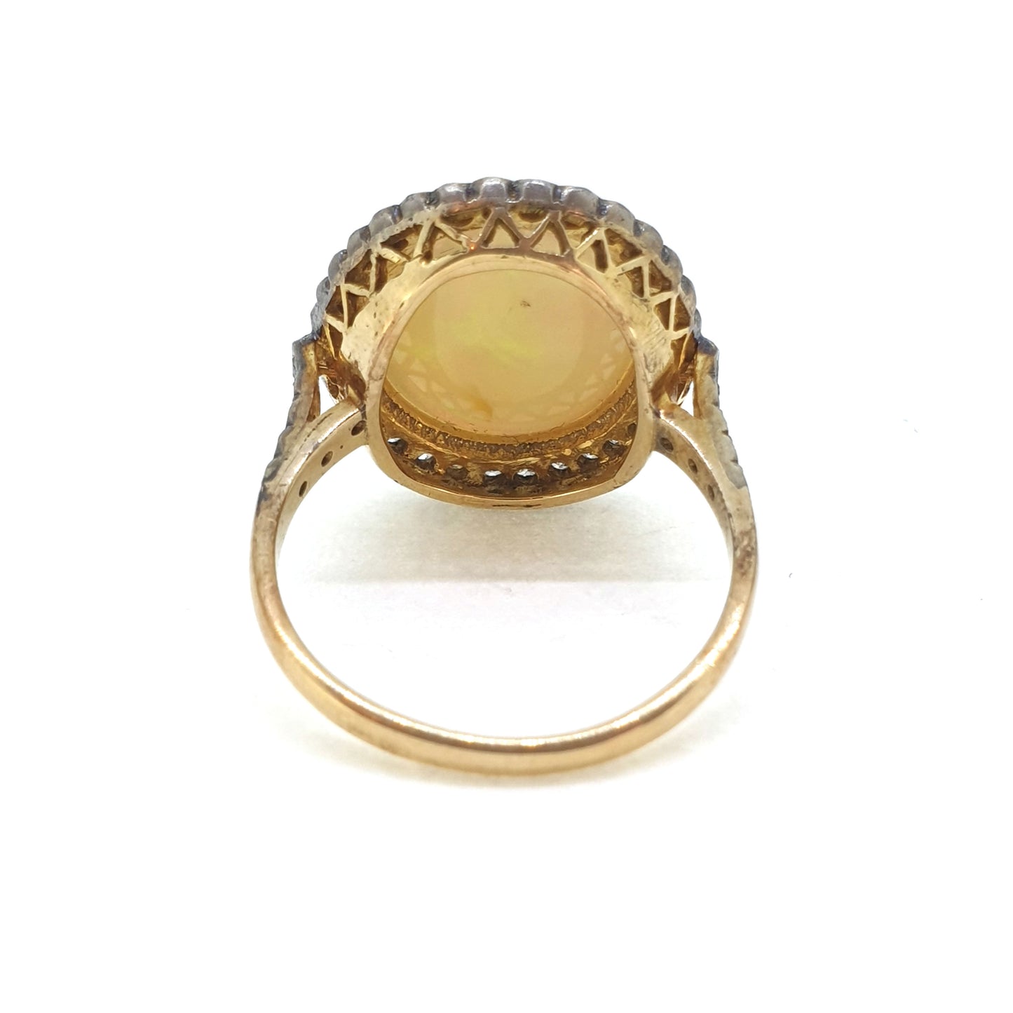 A cabochon opal and diamond oval cluster ring in gold and silver, viewed from behind, on a white background