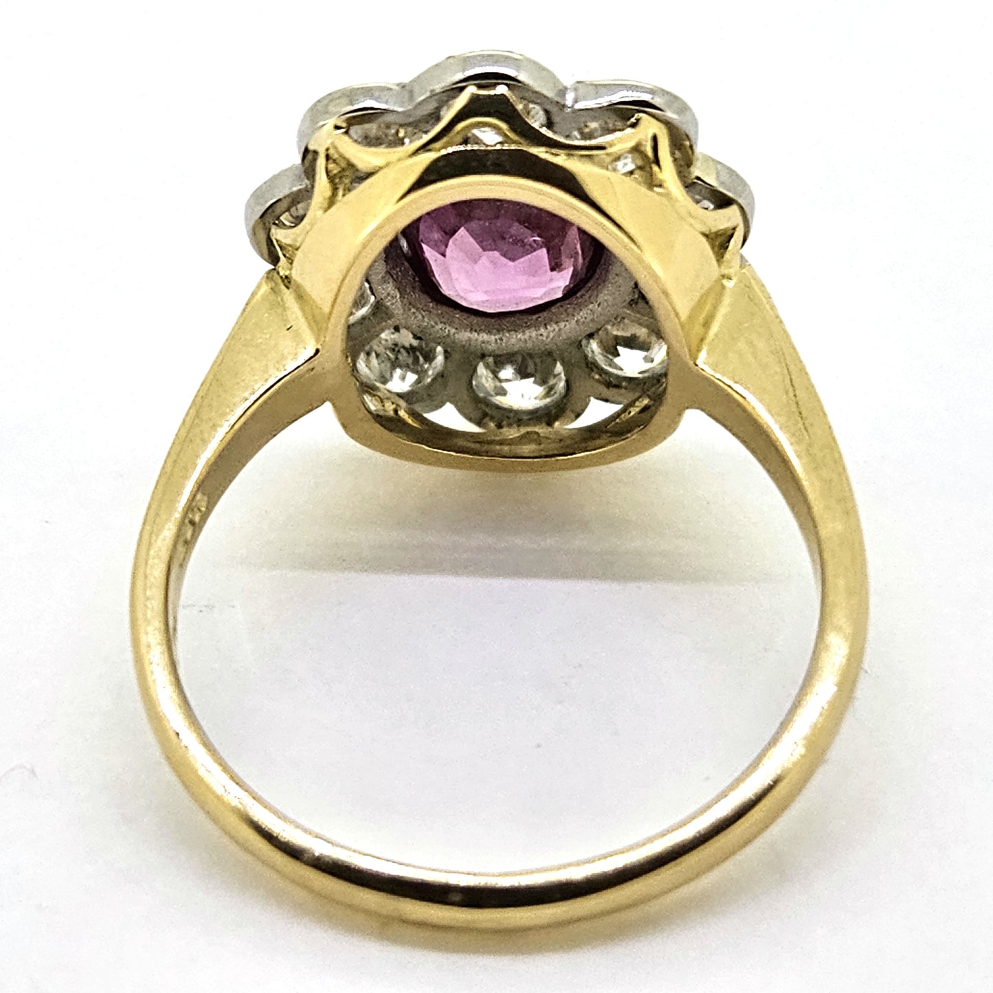 A pink sapphire and round diamond oval shaped cluster ring in yellow and white metal, on a white background