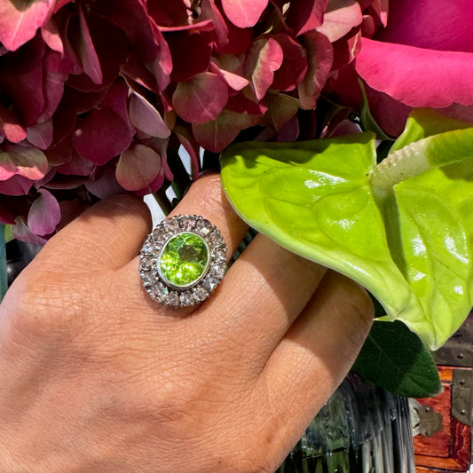 An oval peridot and diamond cluster ring in gold and silver, modelled on a hand, with flowers