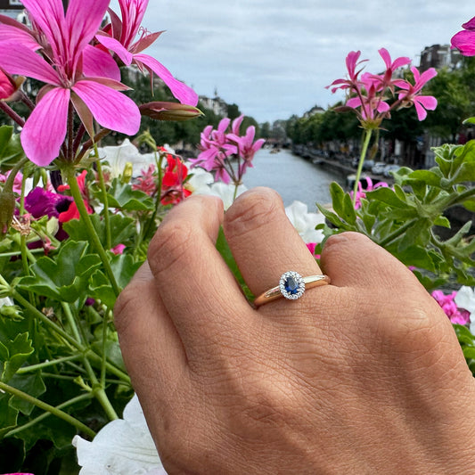 An oval sapphire and diamond cluster ring in yellow and white gold, modelled on a hand