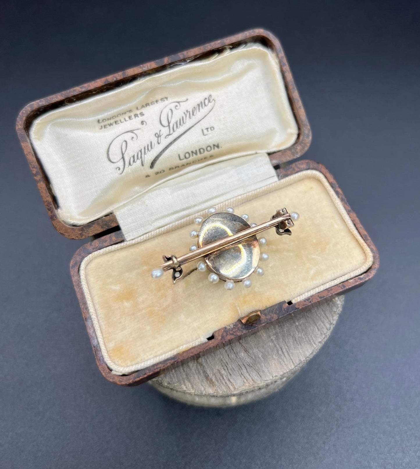 A yellow gold bar brooch with a red enamel centre surrounded by pearls, with a diamond flower motif and diamond leaves at either end, in a box