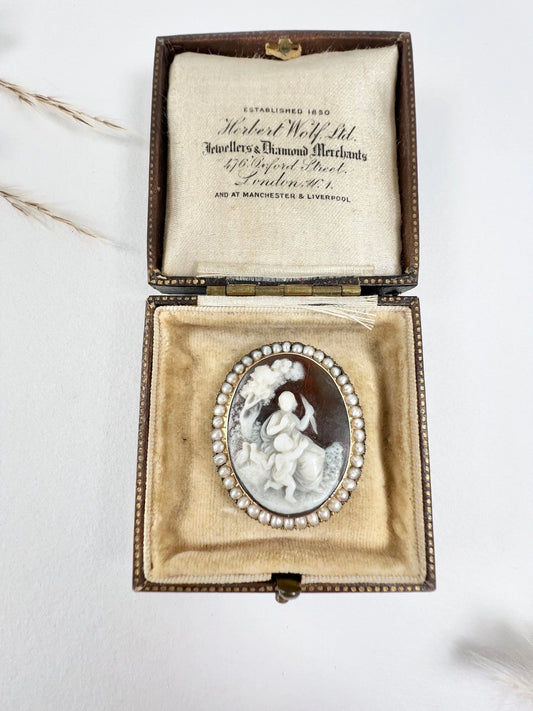 An antique oval cameo brooch depicting cherubs and birds, with a pearl border, set in gold